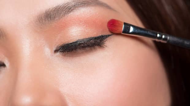 a close up of an Asian woman applying eyeshadow to one eye