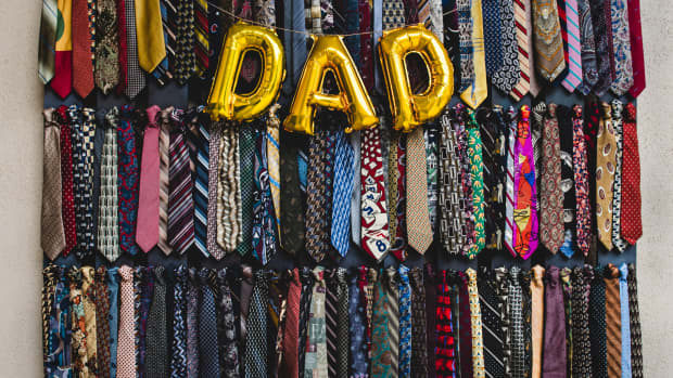 Balloons that spell dad hang on top of a wall full of ties.